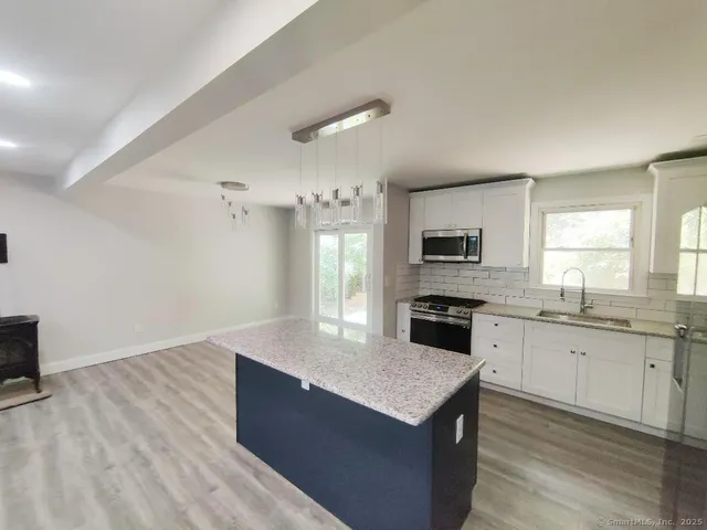 a large kitchen with granite countertop a stove top oven a sink dishwasher and a refrigerator with wooden floor