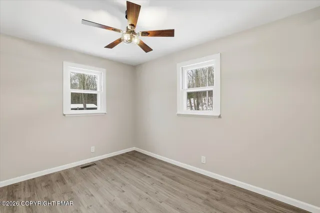 a view of an empty room with wooden floor and a ceiling fan
