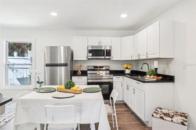 a kitchen with stainless steel appliances kitchen island granite countertop a sink dishwasher a stove a refrigerator a microwave oven with white cabinets and wooden floor