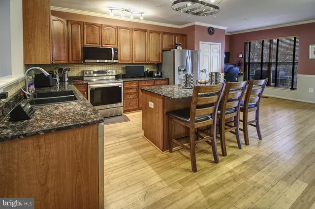 a kitchen with stainless steel appliances granite countertop a stove top oven a sink dishwasher a dining table and chairs with wooden floor