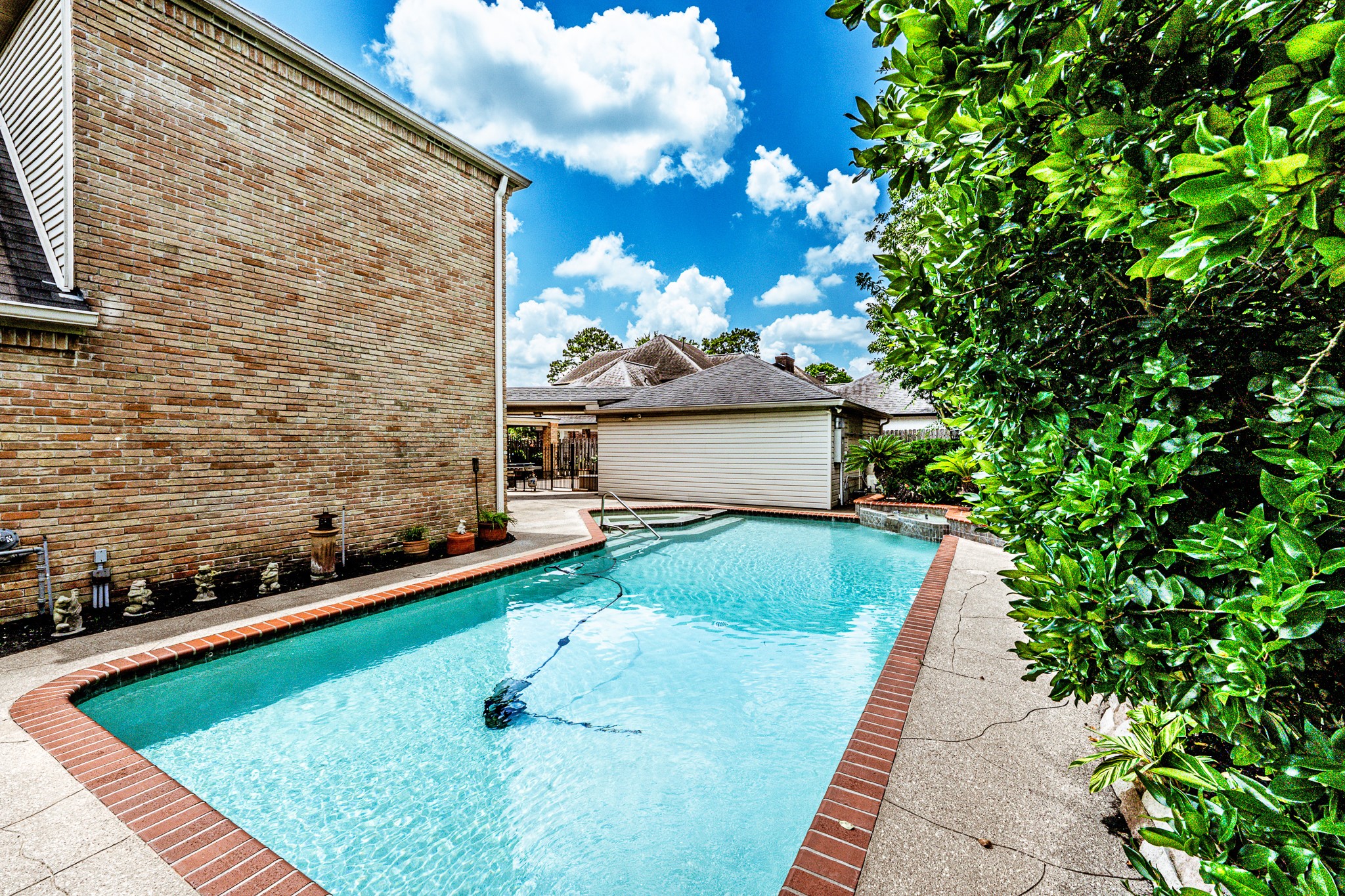 6047 Spring Creek Lane Spring, TX 77379 - Photo 43 of 50 Tucked within the privacy of the courtyard style backyard, the pool offers a quieter setting for cooling off on warm afternoons or unwinding beneath the evening sky. Clean lines, brick surroundings, and mature landscaping give the space a timeless simplicity that complements the home’s Mediterranean influence.