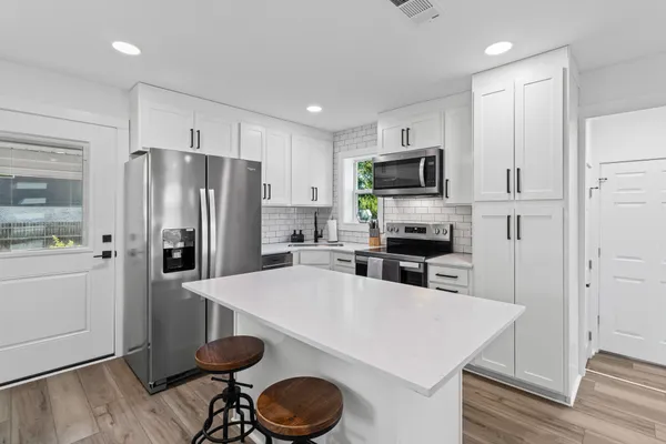 a kitchen with granite countertop a refrigerator oven a sink a stove and white cabinets with wooden floor
