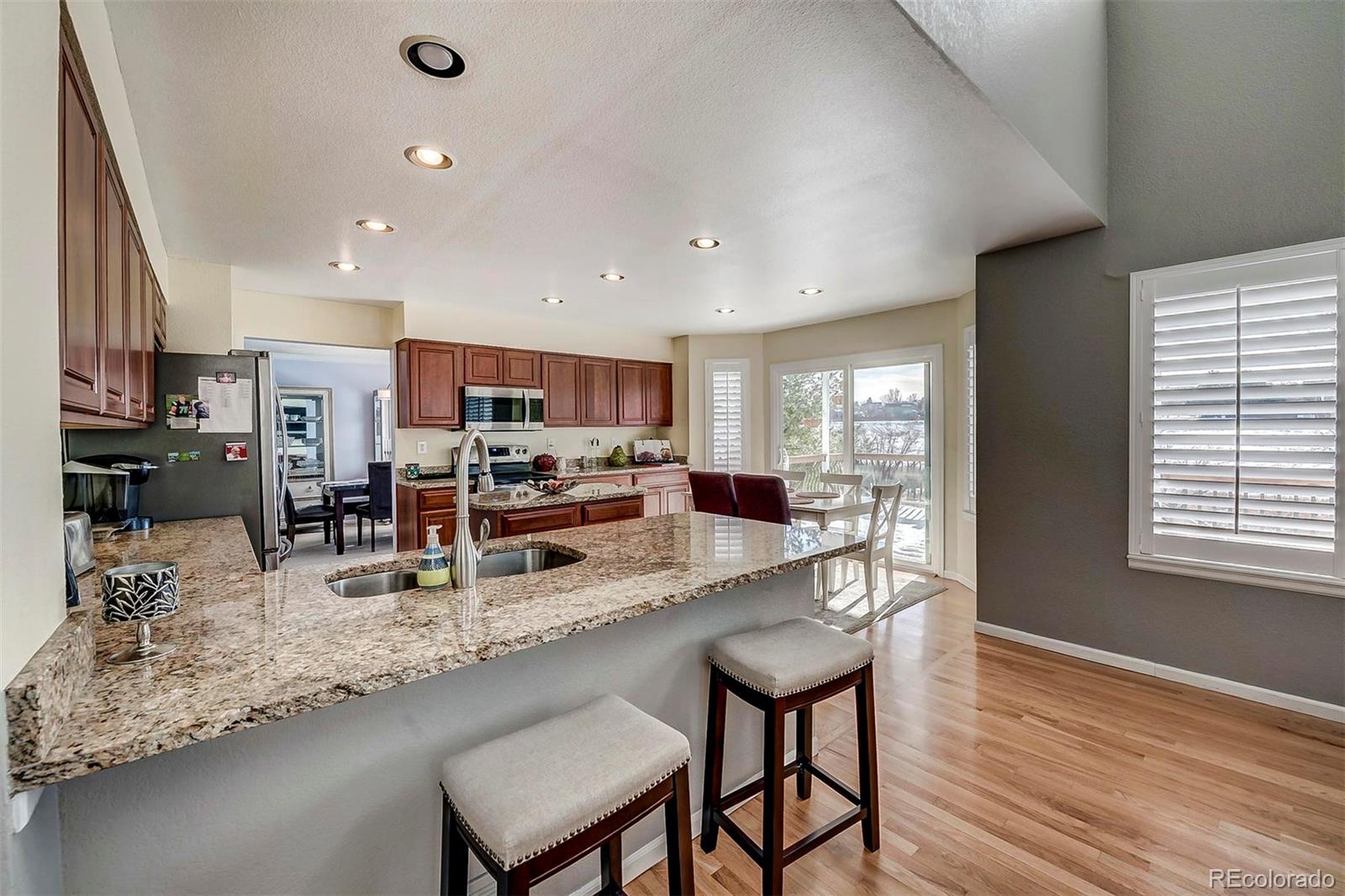 9847 Spring Hill Lane Highlands Ranch, CO 80129 - Photo 20 of 33 a kitchen with stainless steel appliances granite countertop a stove top oven a sink dishwasher a dining table and chairs with wooden floor