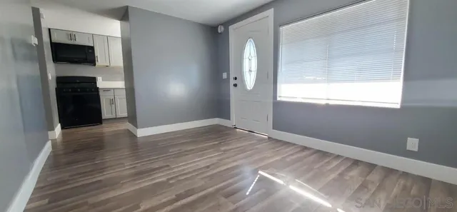 an empty room with wooden floor kitchen view and a window