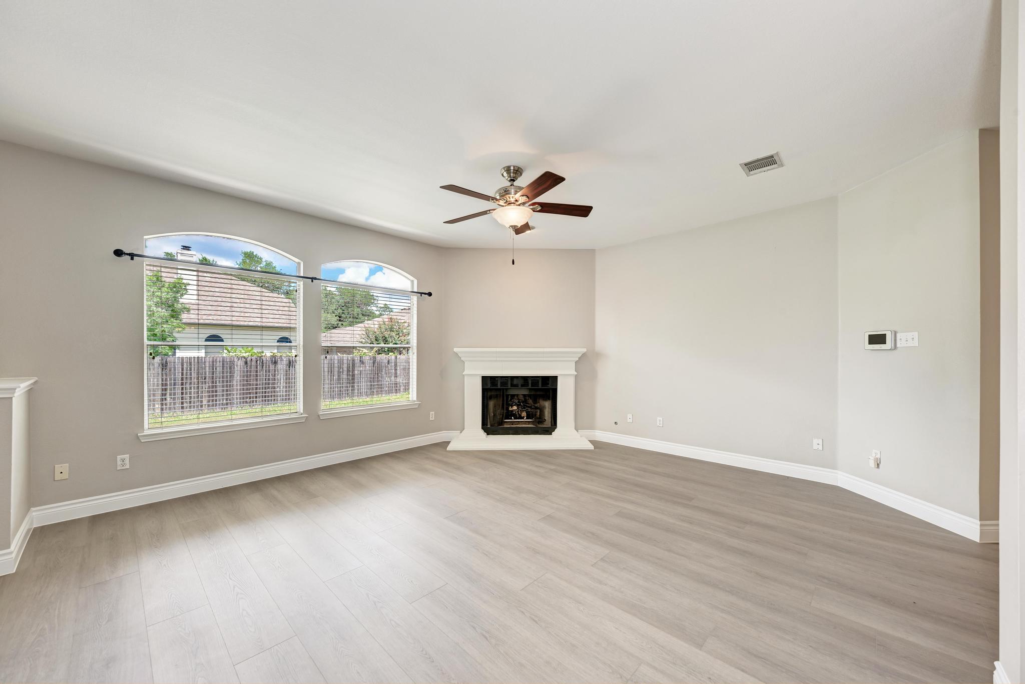 4408 Tello Path Austin, TX 78749 - Photo 9 of 38 Unfurnished living room featuring ceiling fan, light wood-style flooring, and a fireplace with raised hearth