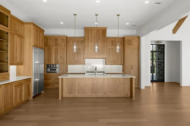 a large kitchen with stainless steel appliances kitchen island granite countertop a refrigerator a stove and a sink with wooden floor