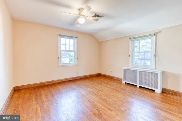 an empty room with wooden floor chandelier fan and windows