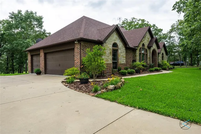 a view of a brick house with a yard plants and large tree