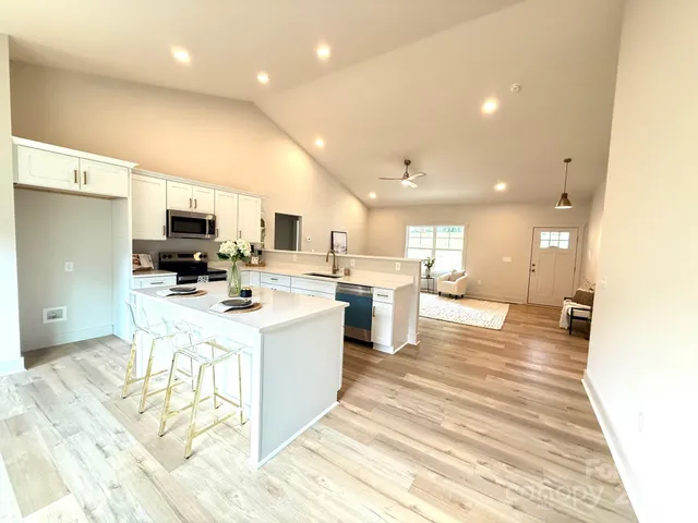 a view of kitchen with stainless steel appliances kitchen island a sink dishwasher a refrigerator and white cabinets with wooden floor