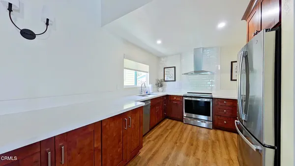 a large kitchen with stainless steel appliances granite countertop a refrigerator a sink dishwasher a stove and white countertops with wooden floor