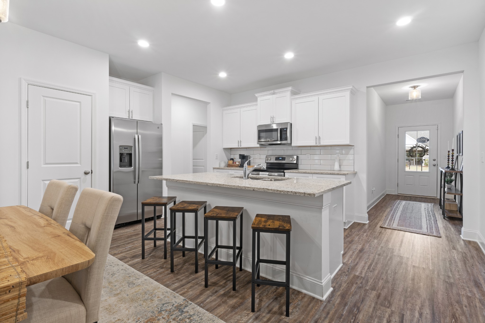 12003 Mdw Pl Lane, Unit 12003 Madison, AL 35757 - Photo 2 of 11 a kitchen with stainless steel appliances granite countertop a table chairs refrigerator a sink a stove a microwave and dining table with wooden floor