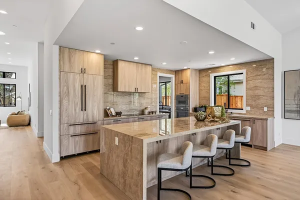 a kitchen with stainless steel appliances granite countertop a stove a sink a refrigerator and white cabinets with wooden floor