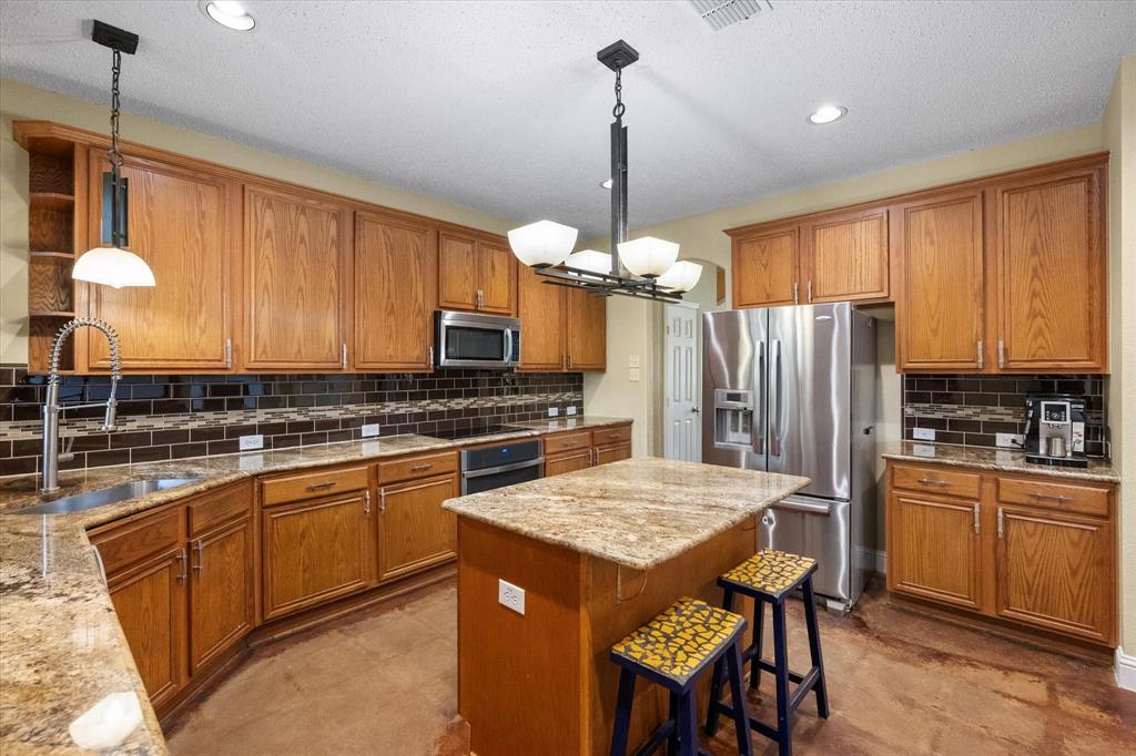 1305 Liverpool Lane Mansfield, TX 76063 - Photo 23 of 40 The kitchen features wooden cabinetry, granite countertops, a tiled backsplash, and stainless steel appliances