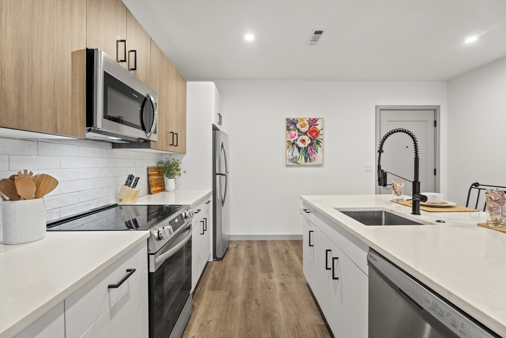 203 Lowell Street, Unit 103 Wilmington, MA 01887 - Photo 4 of 39 a kitchen with stainless steel appliances granite countertop a sink and a stove top oven with wooden floor
