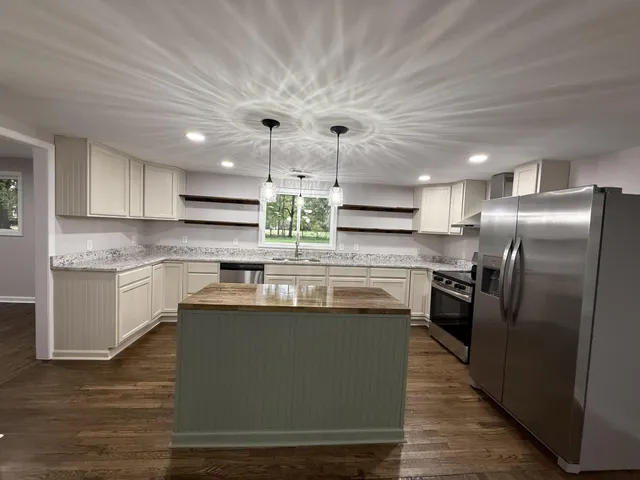 a kitchen with stainless steel appliances granite countertop a sink a stove a refrigerator and island with wooden floor