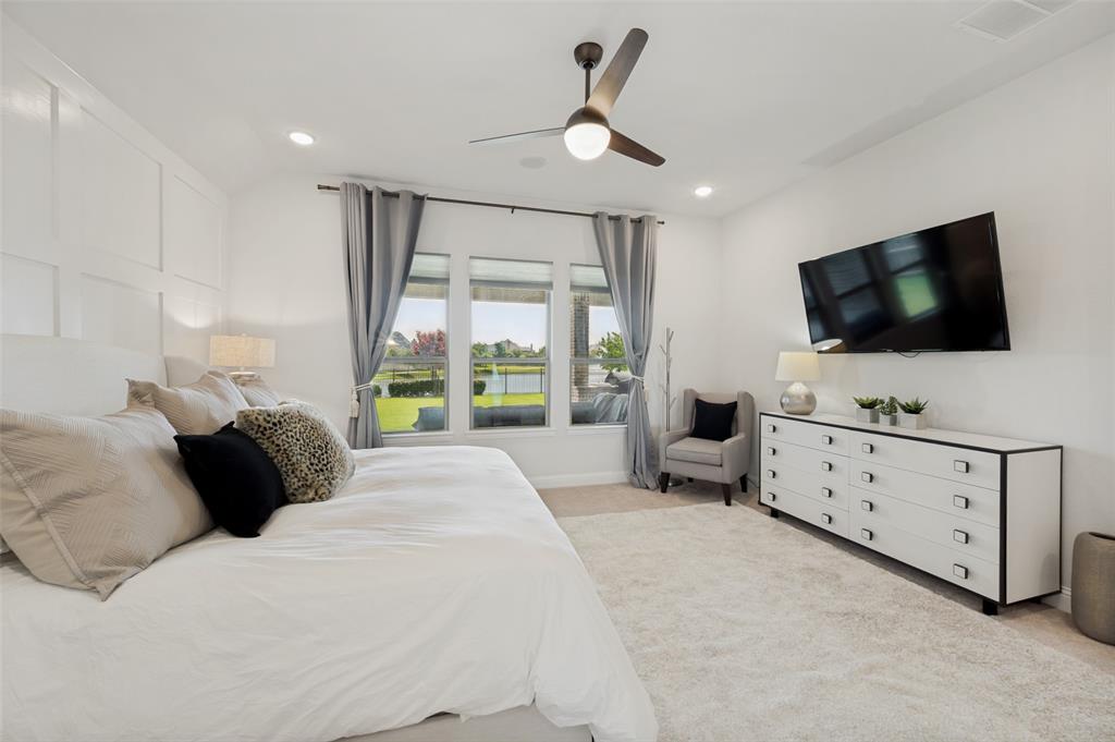 7821 Kentmere The Colony, TX 75056 - Photo 17 of 40 Wake up to tranquil water views from the comfort of the luxurious primary suite. Expansive windows frame the peaceful canal and lush backyard, filling the room with natural light and creating a serene retreat. Plush carpeting, generous proportions, and a modern ceiling fan complete this relaxing sanctuary.