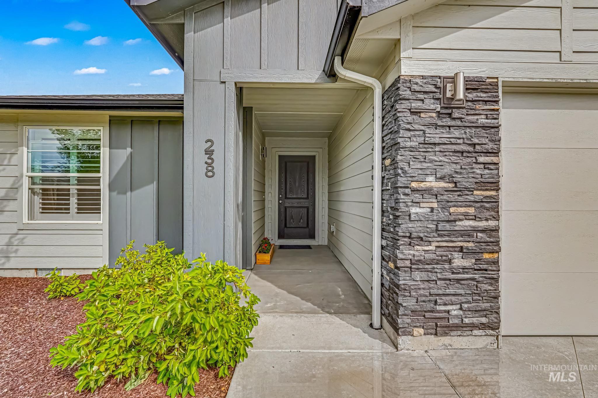 238 West Riggs Spring Avenue Meridian, ID 83642 - Photo 2 of 16 Covered entry with a dark paneled door, vertical siding accents, and a stone veneer column
