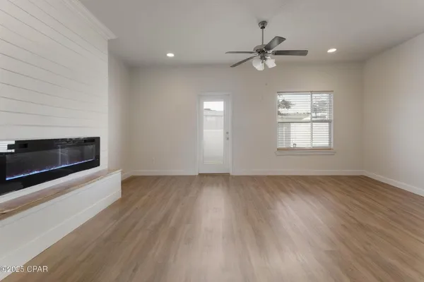 an empty room with wooden floor a ceiling fan and windows