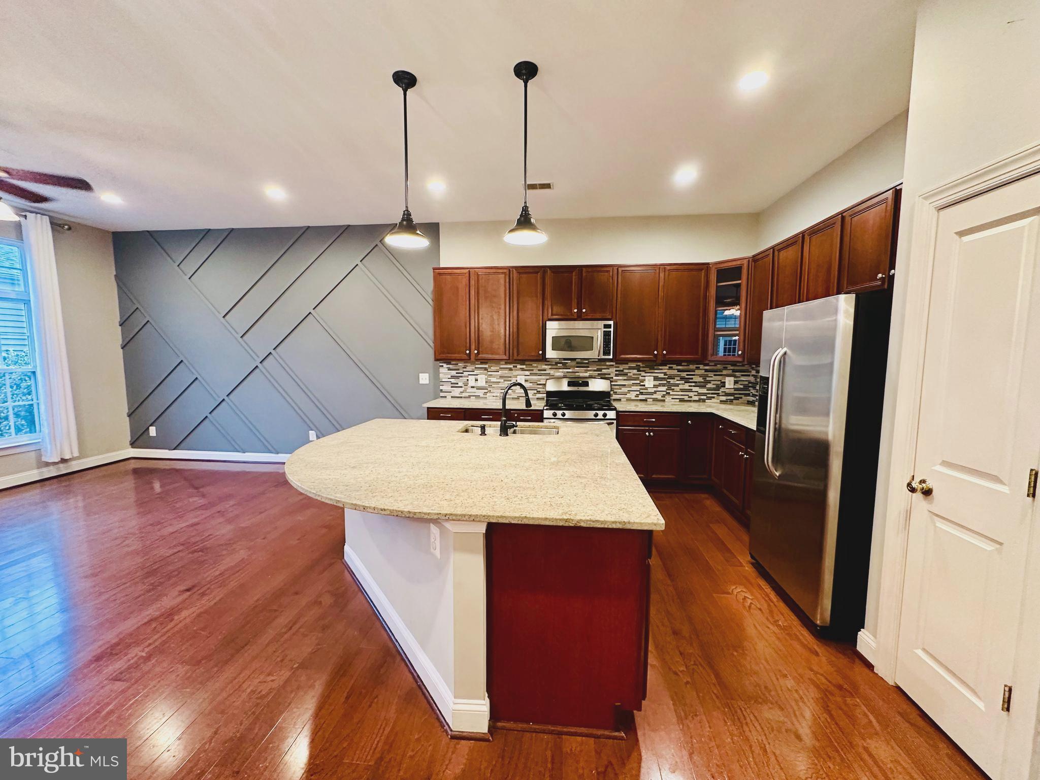 9032 Ribbon Falls Loop Bristow, VA 20136 - Photo 8 of 31 a kitchen with stainless steel appliances kitchen island granite countertop a refrigerator a sink dishwasher a stove and a wooden floor