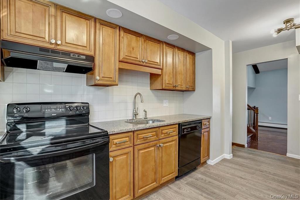 36 Ironworks Road Monroe, NY 10950 - Photo 16 of 37 Kitchen featuring black appliances, light stone countertops, under cabinet range hood, brown cabinetry, and light wood-style flooring