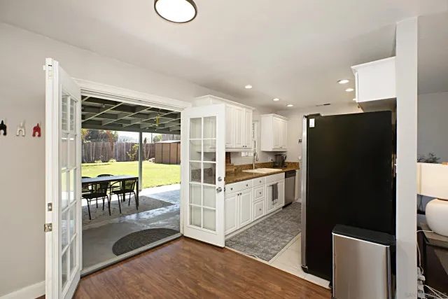 a kitchen with granite countertop a refrigerator a stove a sink and white cabinets with wooden floor