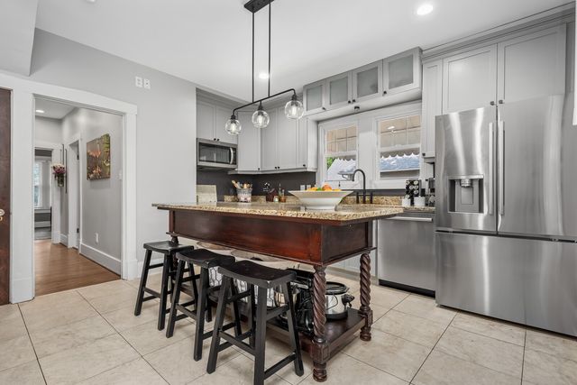 a kitchen with stainless steel appliances granite countertop a sink a stove a refrigerator and a dining table with white cabinets