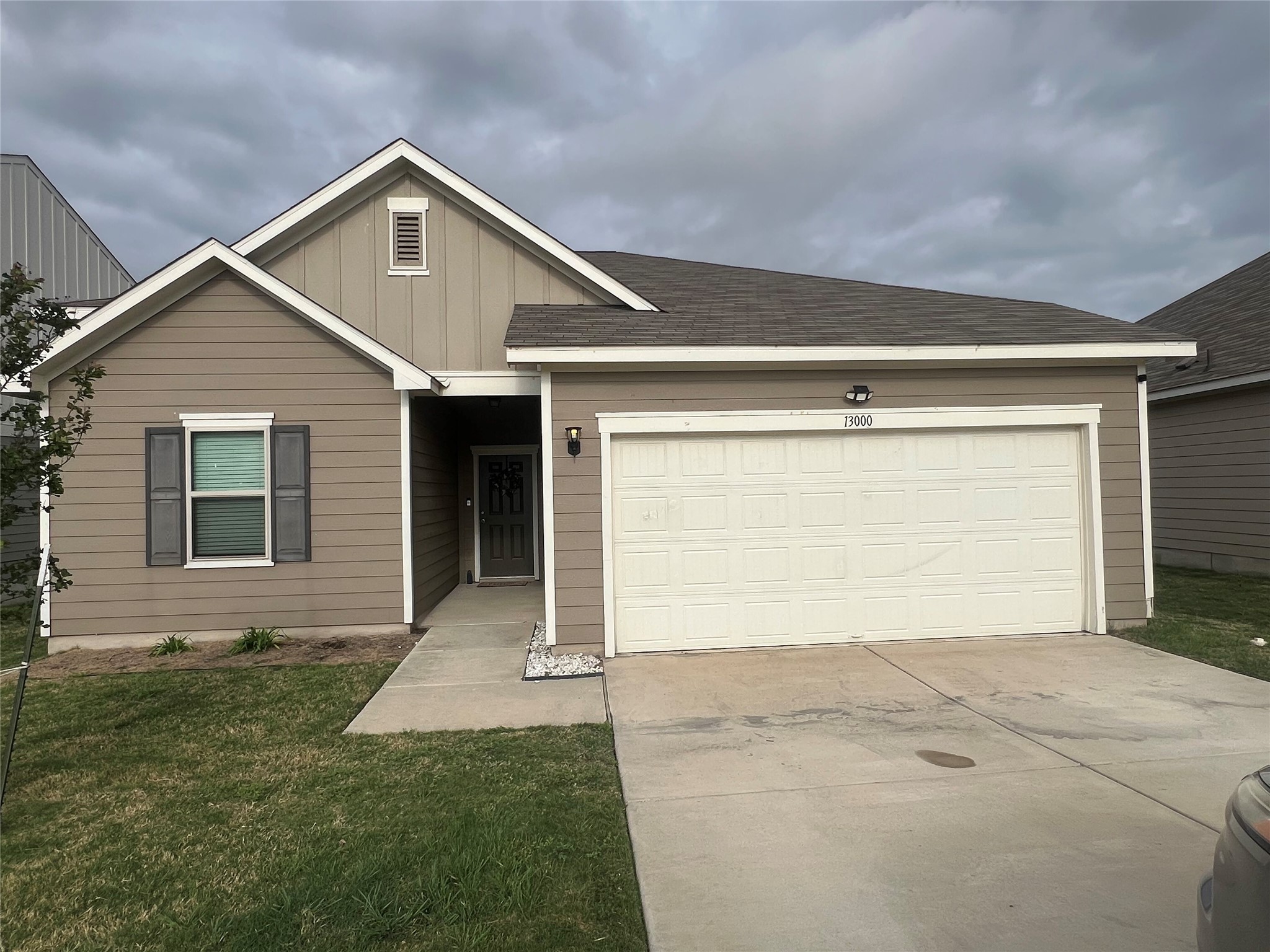 13000 Titanium Street Austin, TX 78754 - Photo 1 of 15 Single-story residence featuring a two-tone facade with tan and light brown siding, a dark asphalt shingle roof, an attached garage with a white panel door, and a concrete driveway