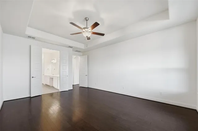 a view of an empty room with wooden floor and a ceiling fan