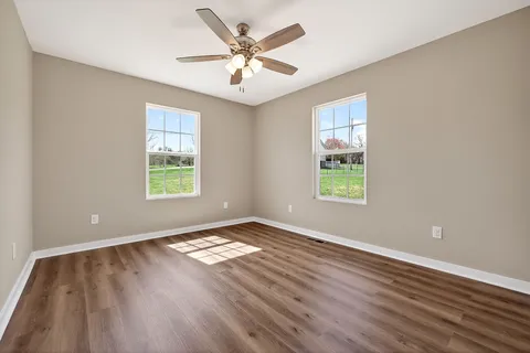 an empty room with wooden floor chandelier fan and windows
