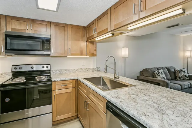 a kitchen with granite countertop a sink dishwasher stove and microwave with wooden cabinets