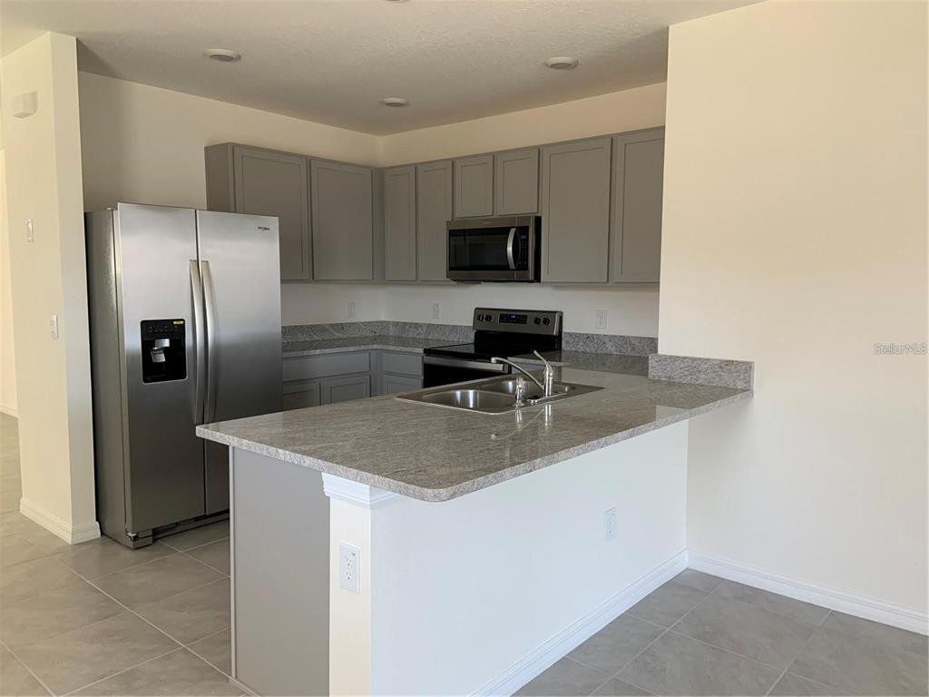5518 Oxford Gray Road Wesley Chapel, FL 33545 - Photo 4 of 11 a kitchen with stainless steel appliances granite countertop a sink a microwave a refrigerator and a stove
