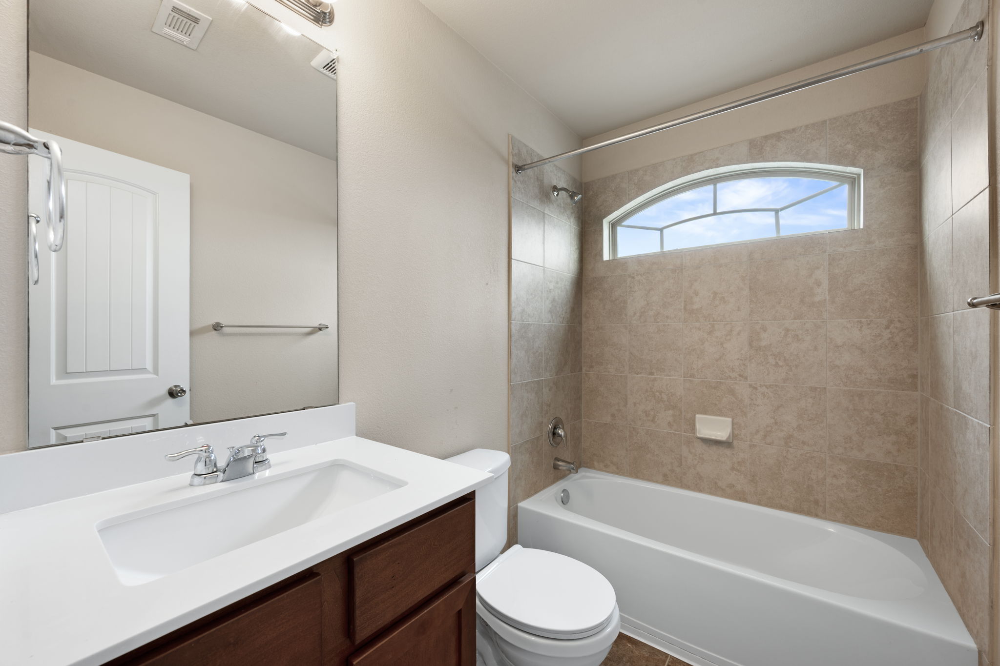 12701 Carillon Way Manor, TX 78653 - Photo 16 of 20 Bathroom featuring a white vanity with a rectangular sink and chrome faucet, a large frameless mirror, a white toilet, and a tiled shower-over-tub with an arched window