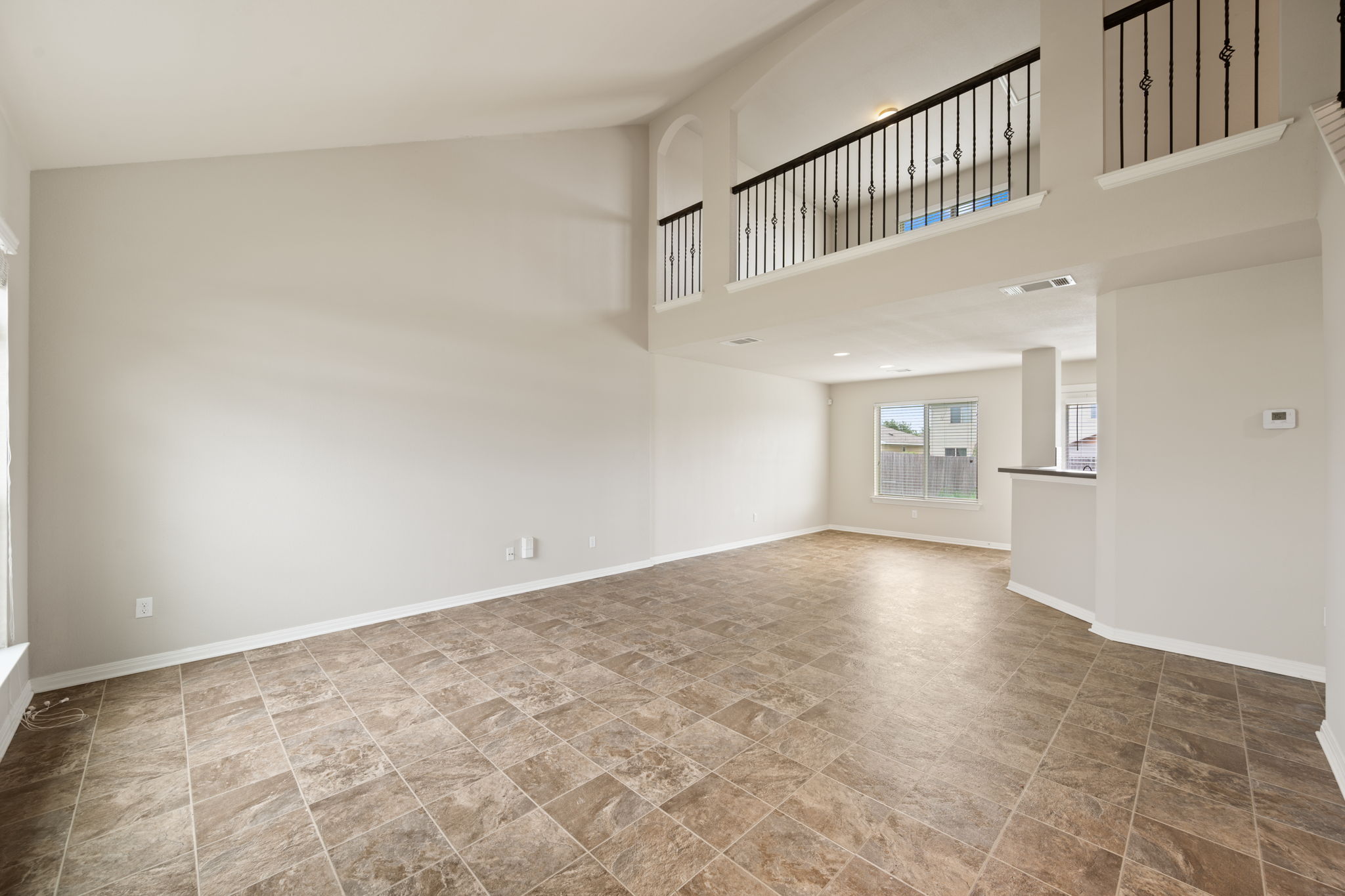 12701 Carillon Way Manor, TX 78653 - Photo 2 of 20 Spacious open-concept interior featuring light-toned walls, tile flooring, and a two-story ceiling with a second-floor balcony overlooking the main living area
