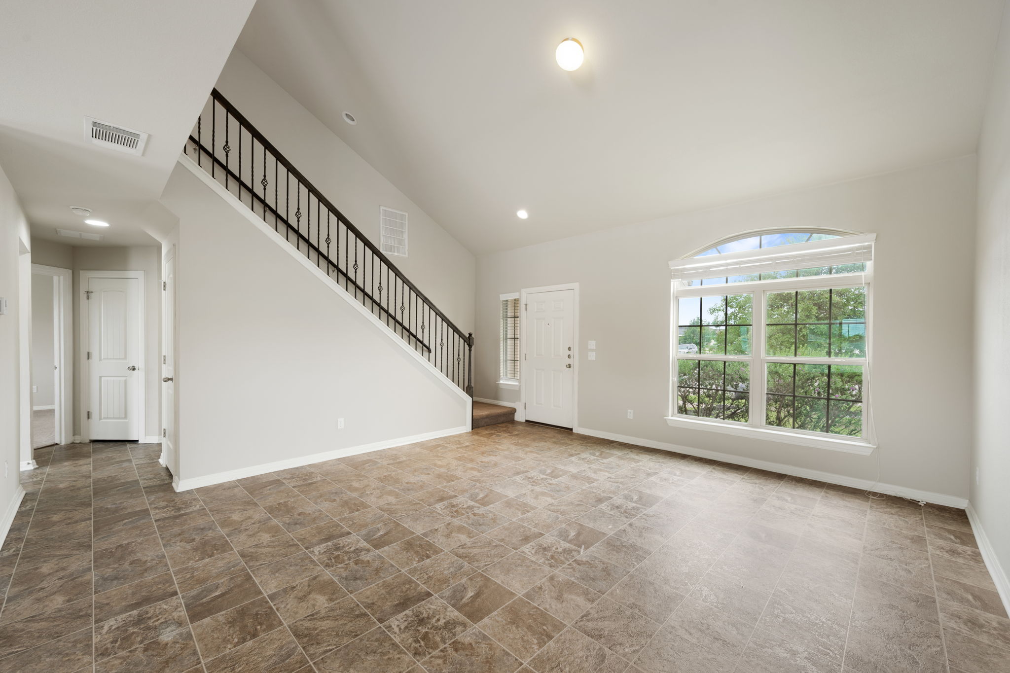 12701 Carillon Way Manor, TX 78653 - Photo 3 of 20 Inviting entry space featuring tile flooring, a prominent staircase with wrought iron balusters, a paneled front door, and a large arched window