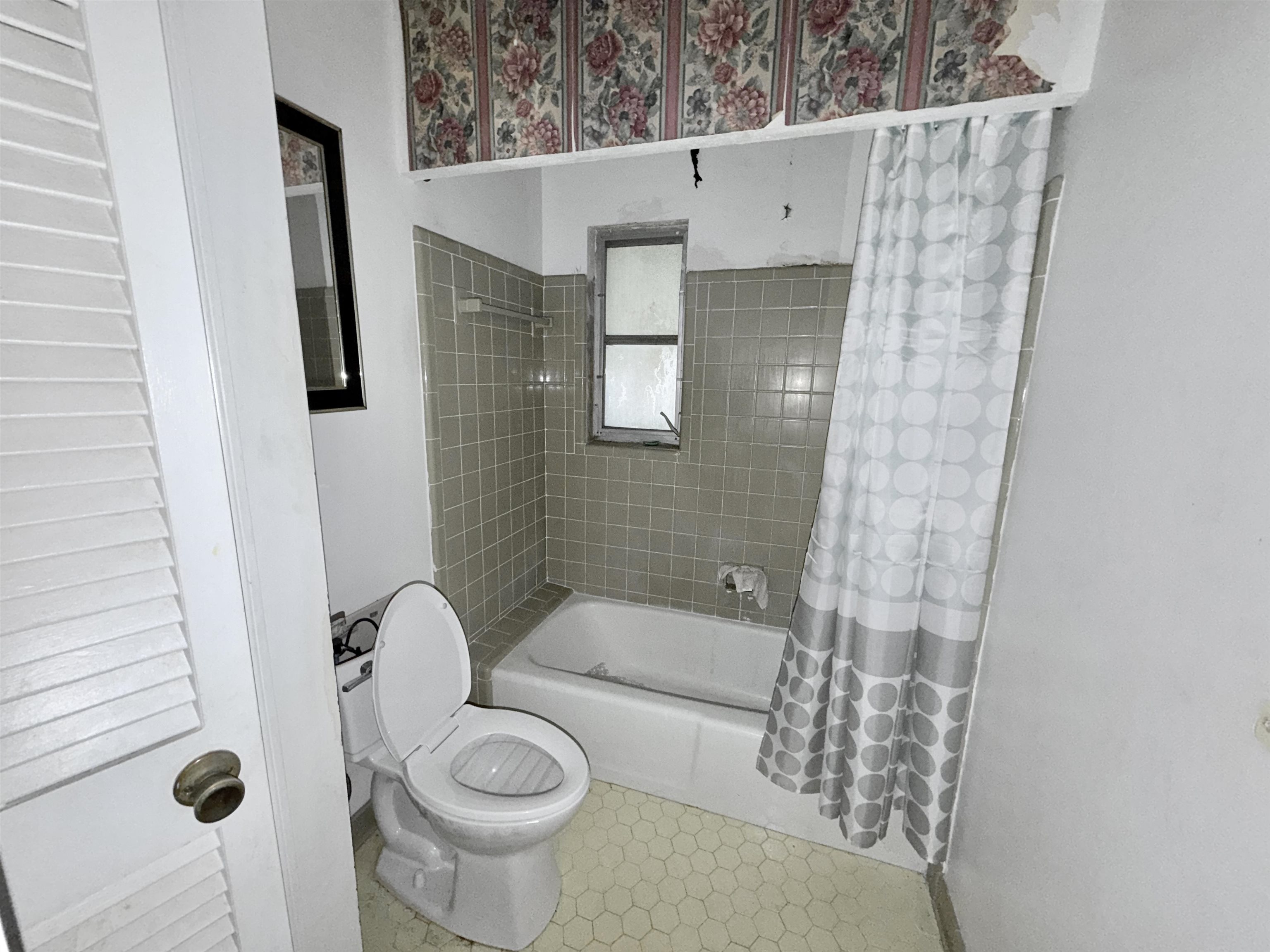 5536 Cottonwood Road Memphis, TN 38115 - Photo 10 of 28 Bathroom featuring a white porcelain toilet, a built-in bathtub with tiled surround, a louvered door, a framed mirror, and hexagonal floor tiling