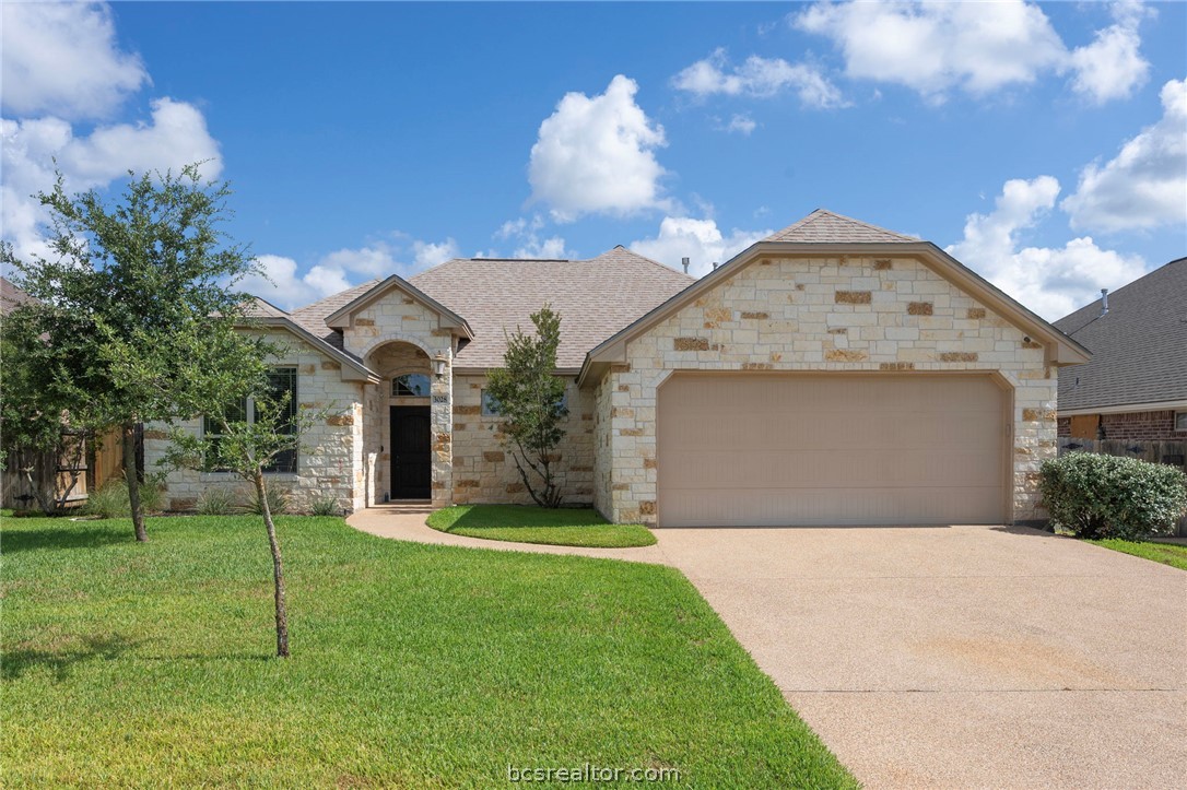 French country style house with stone siding, a front lawn, concrete driveway, and an attached garage
