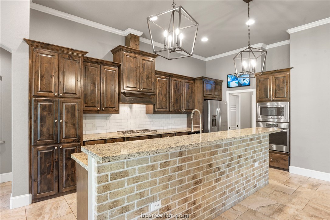 3028 Embers Loop Bryan, TX 77808 - Photo 6 of 26 Kitchen featuring dark brown cabinets, hanging light fixtures, backsplash, stainless steel appliances, and light stone counters
