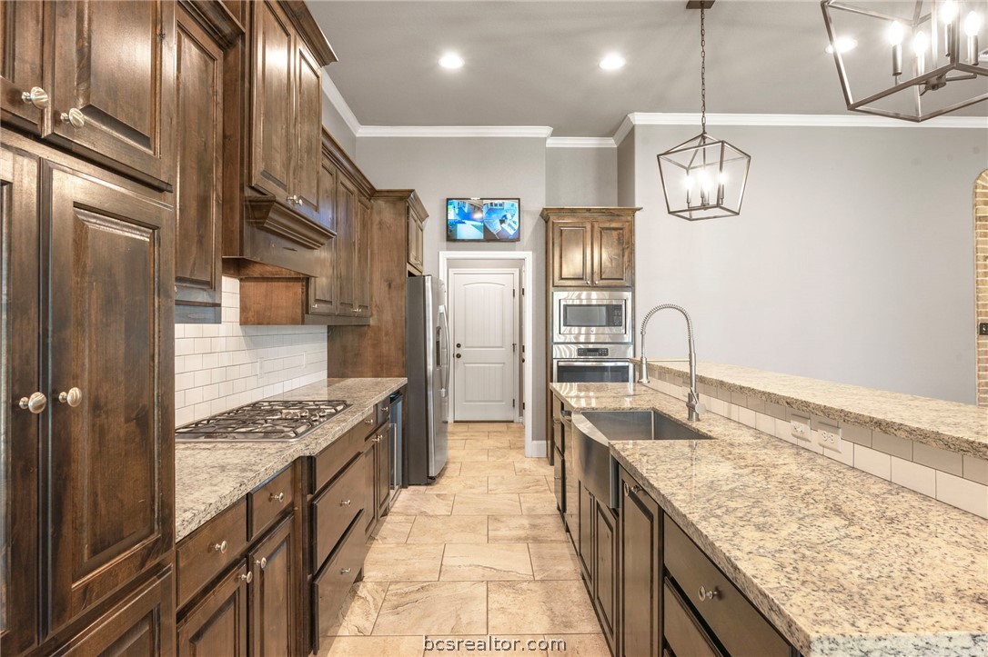 3028 Embers Loop Bryan, TX 77808 - Photo 7 of 26 Kitchen with backsplash, crown molding, hanging light fixtures, light stone counters, and stainless steel appliances