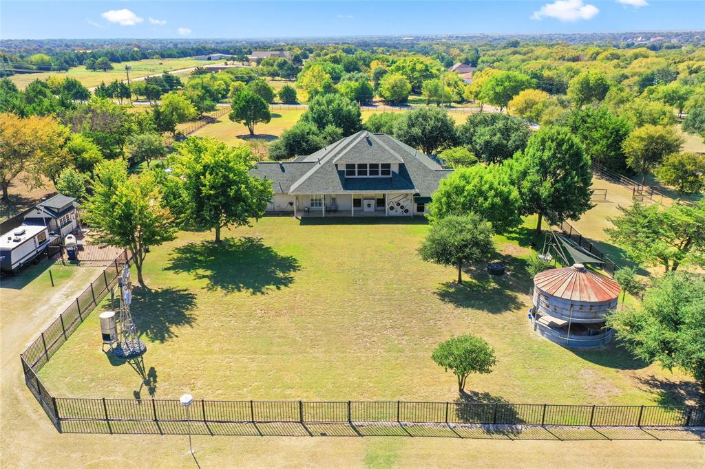 4451 Shiloh Road Midlothian, TX 76065 - Photo 34 of 39 Aerial view of backyard. This photo shows features the gazebo, swing set, and the fenced in area for the family. Behind the fence toward the bottom of the photo is the pasture. The windmill and pump in this photo are only decorative. The gazebo is a 1955 18’ grain silo that was made into an outdoor kitchen. This area has a cement floor with available water. House is wire and plumbed for a pool. The house has two 20 Amp electrical circuits near on the exterior rear of the house for a future swimming pool. The house has 1” copper pipe for a future grill. Solar screens on most windows of home.