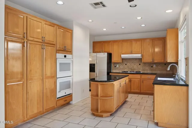 a kitchen with stainless steel appliances granite countertop a refrigerator a stove and a sink with couches