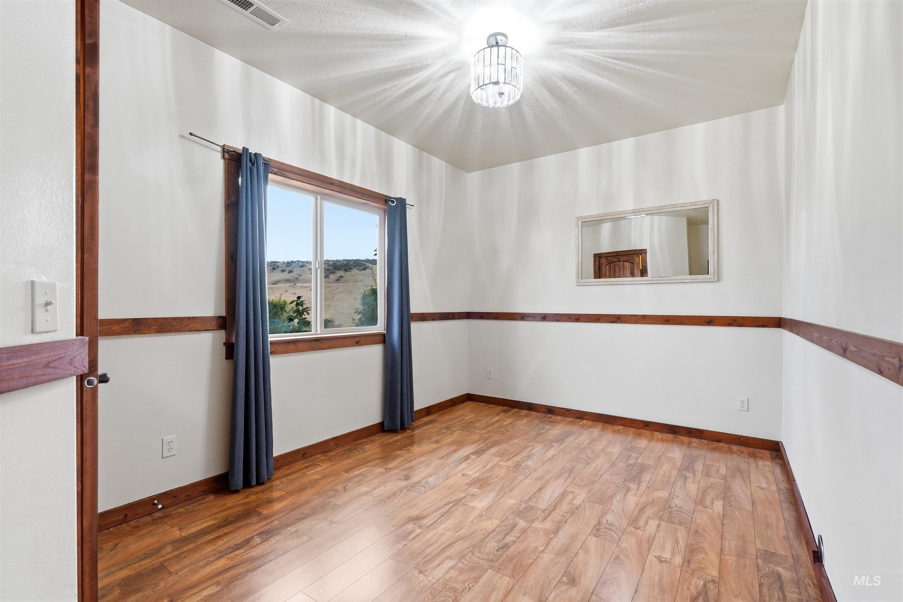 3645 Butte Road Emmett, ID 83617 - Photo 31 of 39 Wood-finish flooring, white walls with natural wood trim, window with an exterior landscape, and a decorative ceiling light fixture