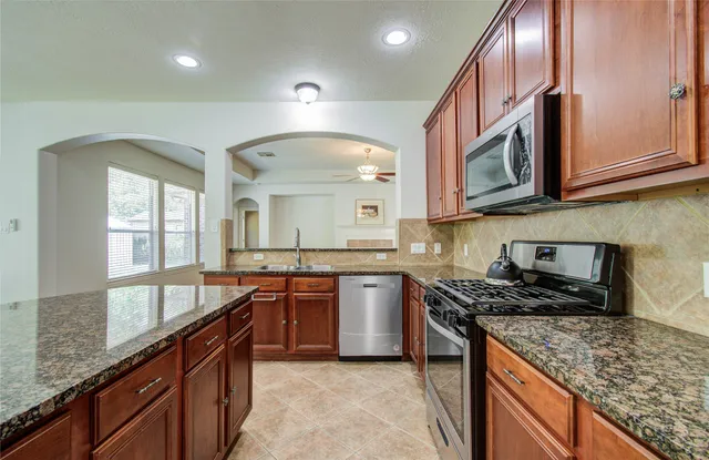 a kitchen with stainless steel appliances granite countertop a sink a stove and a wooden cabinets