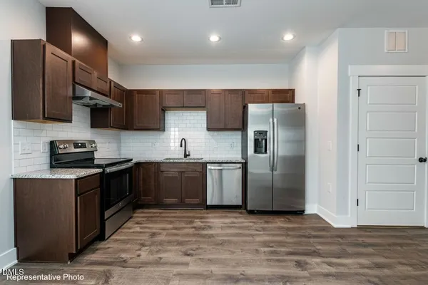 a kitchen with stainless steel appliances granite countertop a refrigerator a sink a stove and a refrigerator with wooden floor
