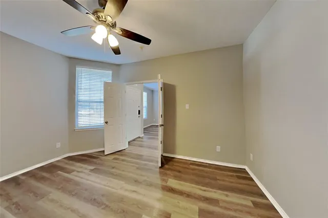an empty room with wooden floor chandelier fan and windows