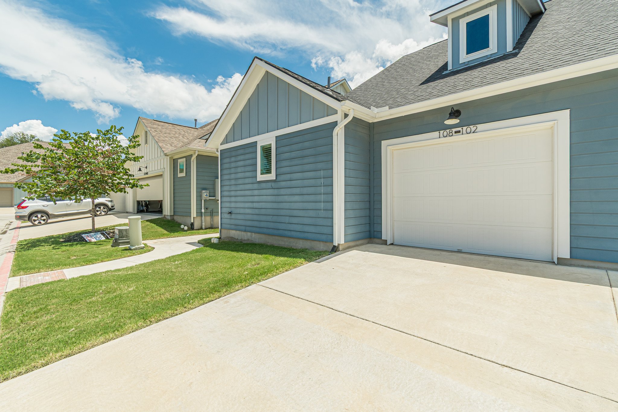 108 Lafitte Drive, Unit 102 San Marcos, TX 78666 - Photo 24 of 27 View of side of property featuring driveway, board and batten siding, an attached garage, a lawn, and roof with shingles