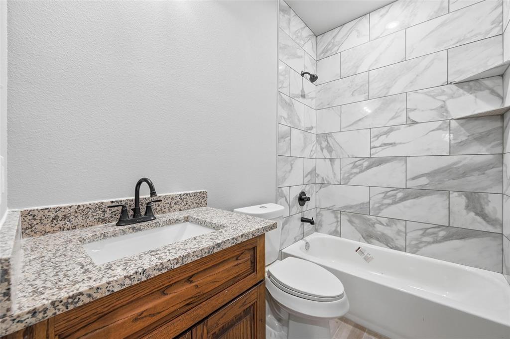 308 Lewis Street Cleburne, TX 76031 - Photo 12 of 20 a bathroom with a granite countertop sink a toilet and bathtub