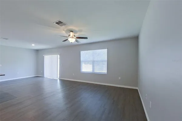 an empty room with wooden floor chandelier fan and windows