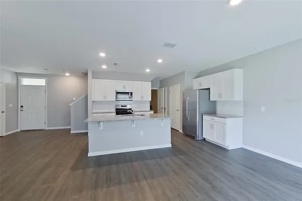 a view of kitchen with kitchen island a sink wooden floor white stainless steel appliances and cabinets