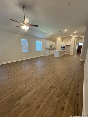 an empty room with wooden floor a ceiling fan and kitchen view