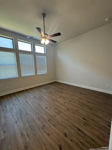 an empty room with wooden floor fan and windows